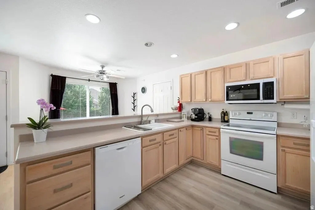Kitchen featuring light wood cabinetry, white appliances, a stainless steel sink, and wood-finish flooring
