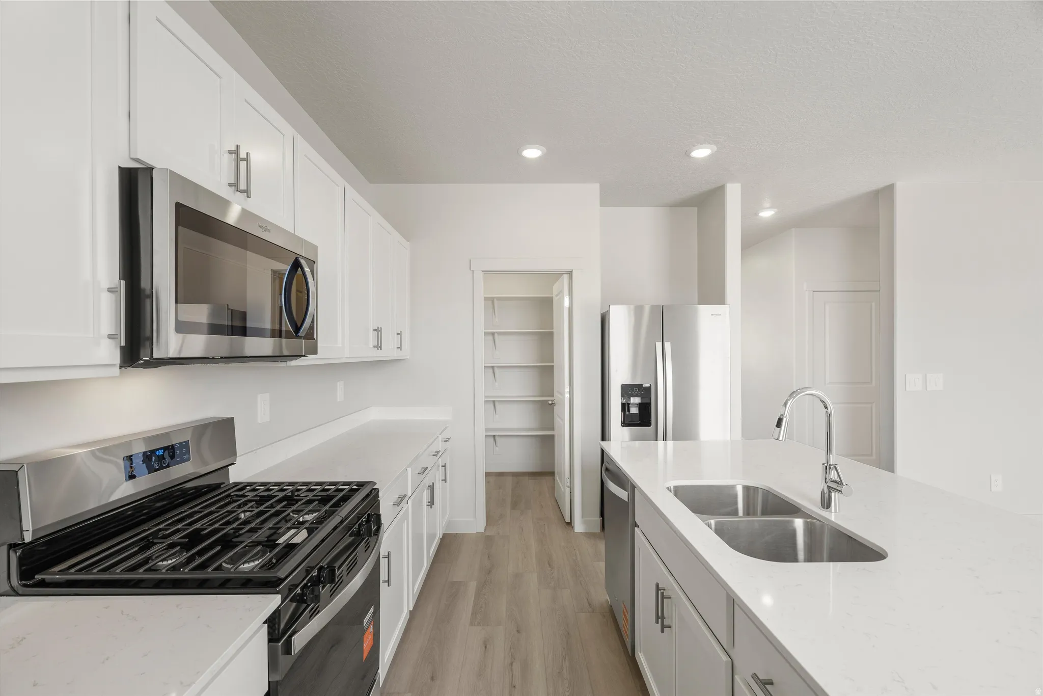 Modern kitchen with white cabinetry, stainless steel appliances, light-toned countertops, a gas range, and a walk-in pantry