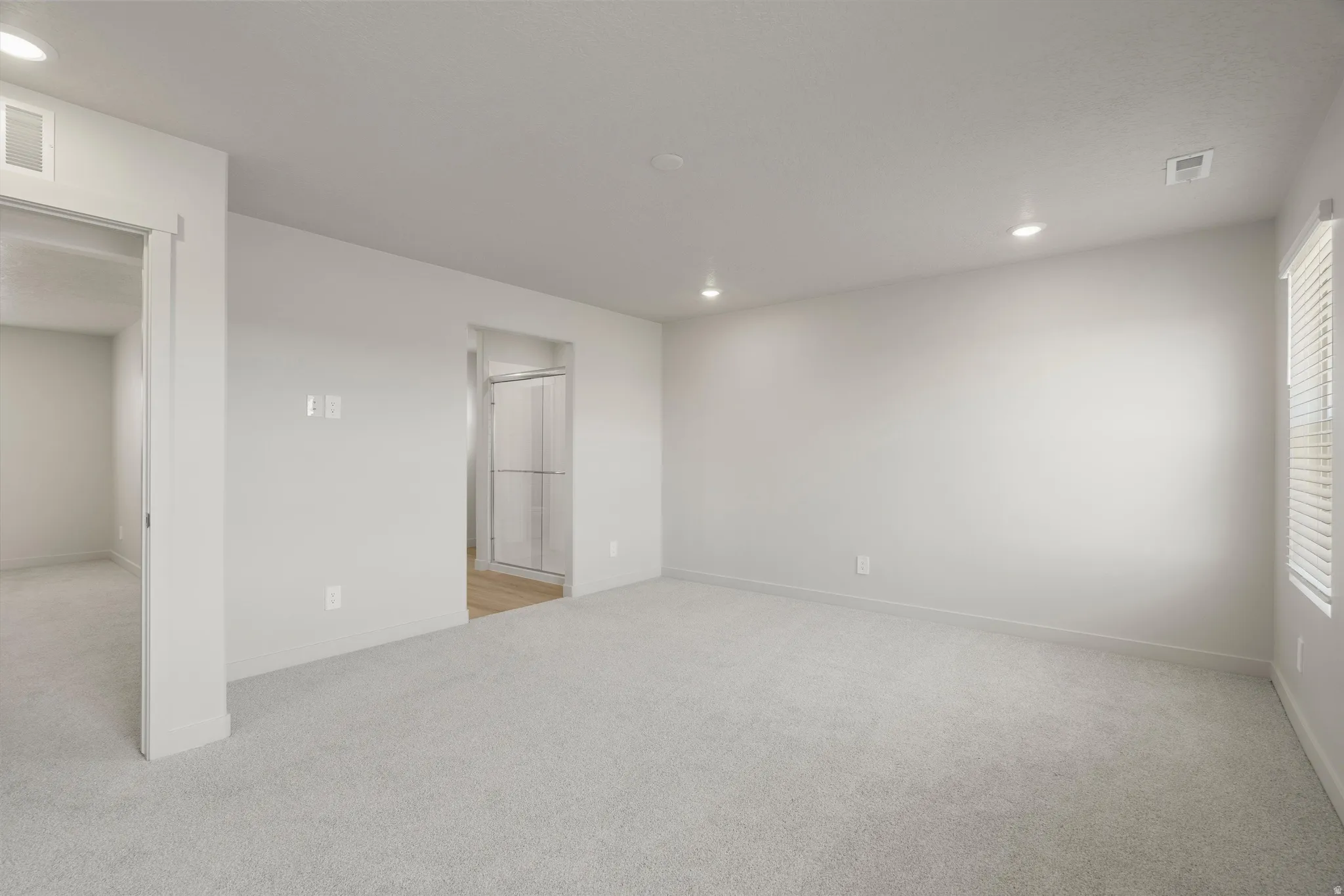 Spacious room featuring light gray carpeting, recessed lighting, and white walls