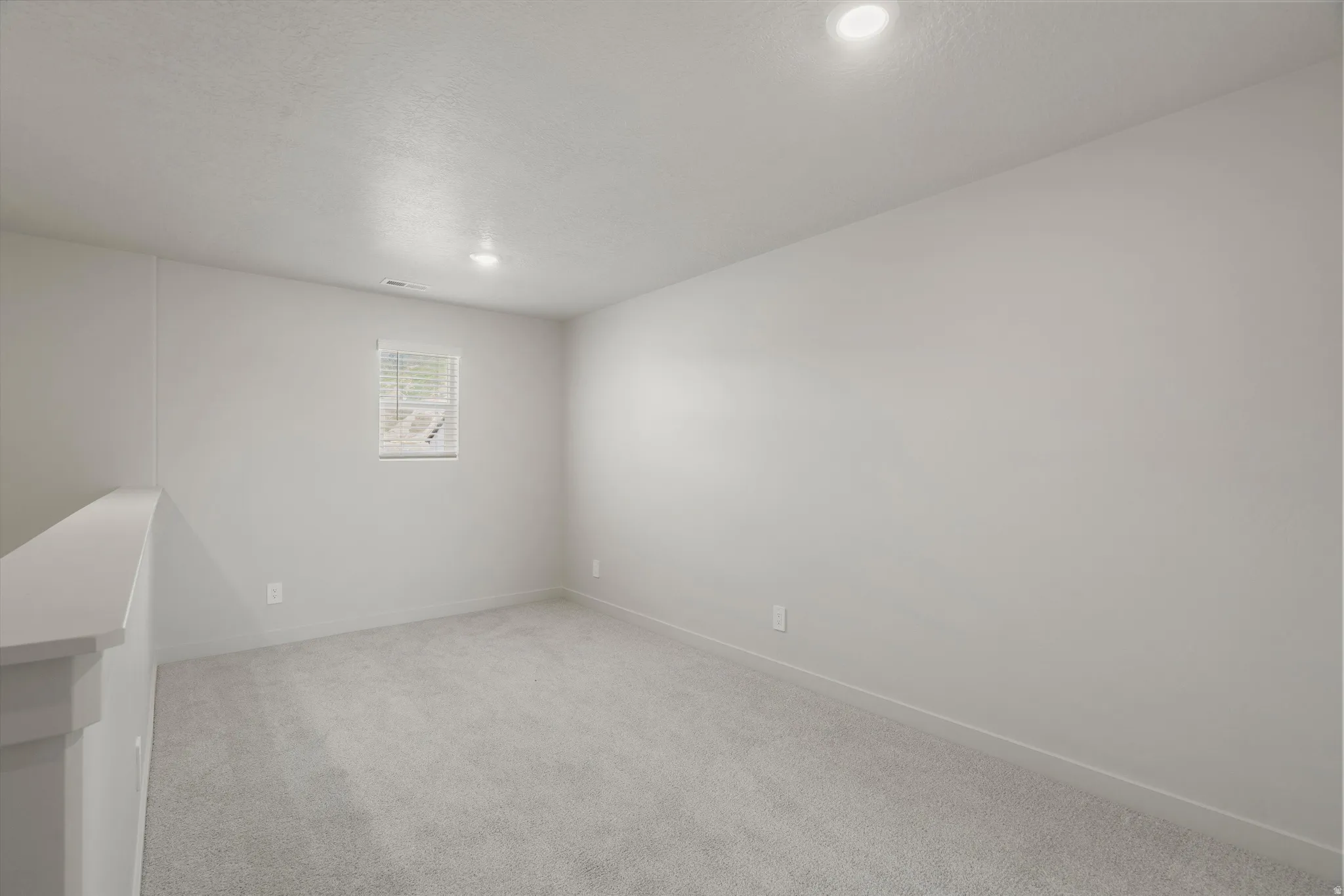 Carpeted room featuring a single window with blinds, recessed ceiling lighting, and light-toned wall paint