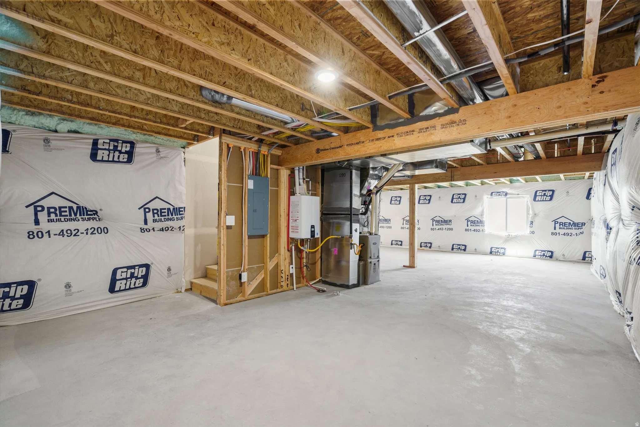Unfinished basement space with exposed wood joists, concrete flooring, and a tankless water heater