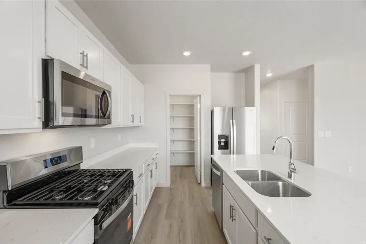 Modern kitchen with white cabinetry, stainless steel appliances, light-toned countertops, a gas range, and a walk-in pantry