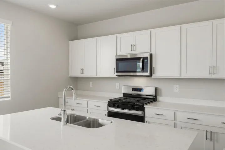 Kitchen featuring white shaker cabinetry, stainless steel appliances, a dual basin sink, and ample countertop space