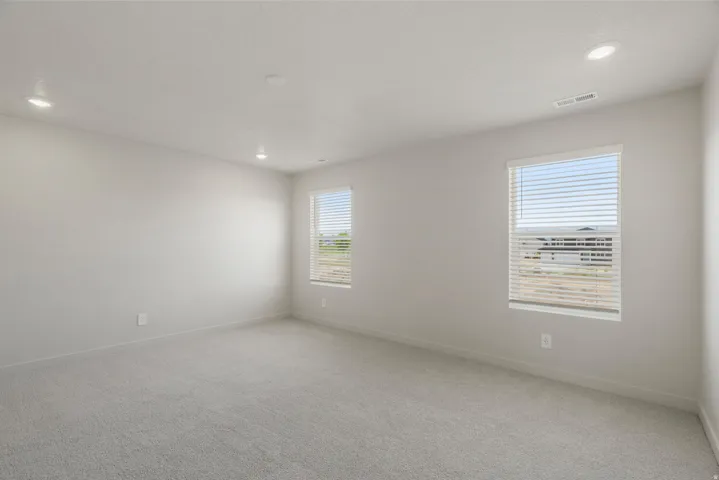 Spacious room featuring neutral carpeting, recessed lighting, and two windows with blinds