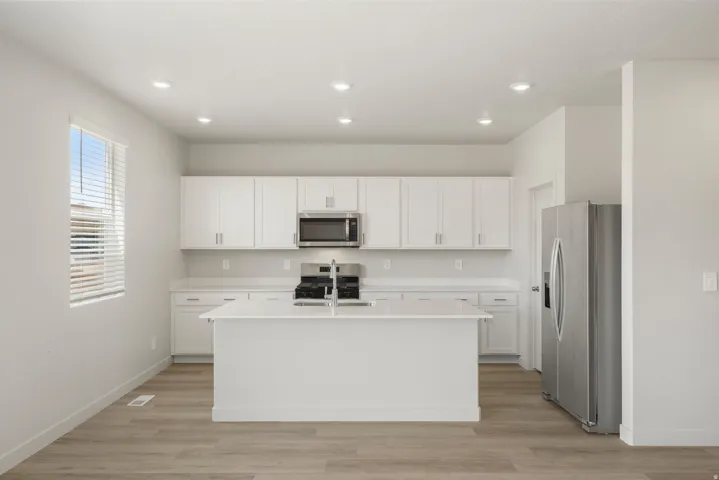 Contemporary kitchen featuring a central island, white cabinetry, stainless steel appliances, recessed lighting, and wood-finish flooring