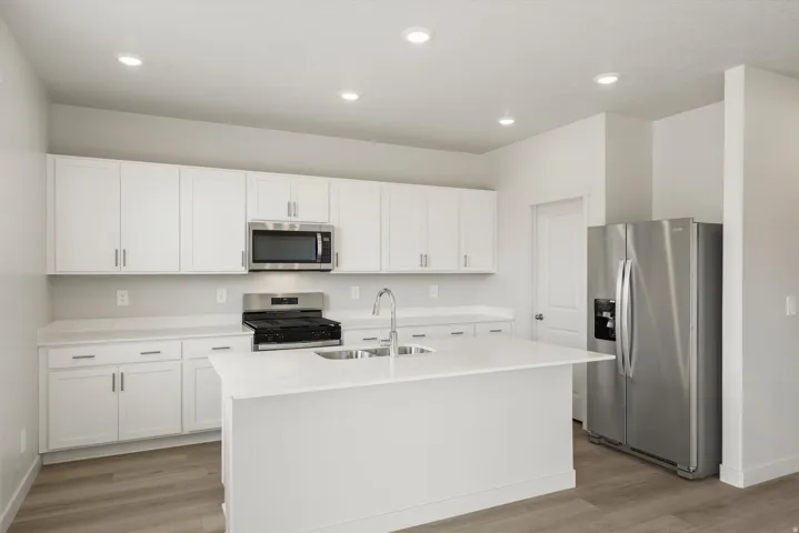 Contemporary kitchen featuring an island with an undermount sink, white cabinetry, integrated stainless steel appliances, light-toned countertops, and wood-finish flooring