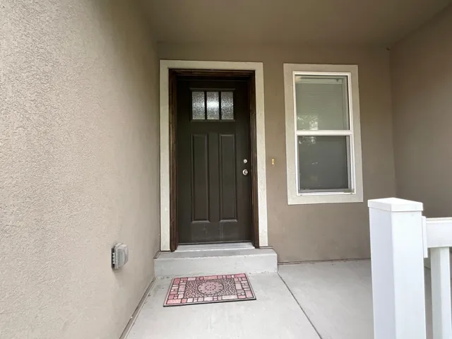 Entryway featuring a dark paneled door with decorative glass inserts, stucco exterior, concrete porch, and a vertical window with white trim