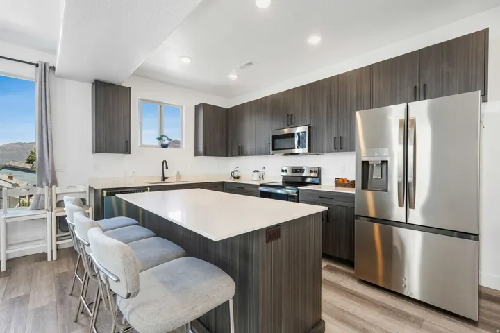 Modern kitchen featuring a large central island with seating, stainless steel appliances, dark wood-finish cabinetry, light countertops, and wood-finish flooring