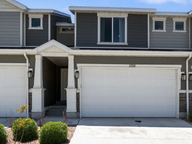Contemporary townhome exterior featuring a neutral gray and white facade, prominent gable rooflines, multiple windows on the upper level, and a two-car garage with white doors