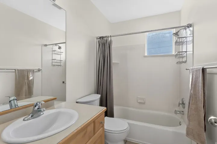 Bathroom featuring a vanity with a light-toned countertop and integrated sink, a full-width wall mirror, a toilet, and a combination shower/tub with a window