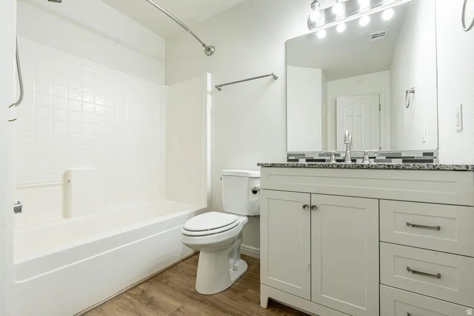 Bathroom featuring wood-finish flooring, a white vanity with shaker-style cabinetry, and a stone-finish countertop