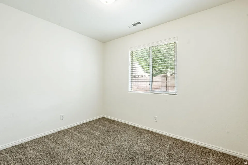 Neutral-toned room featuring a single window with horizontal blinds, textured wall finishes, a ceiling-mounted light fixture, white baseboards, and a carpeted floor
