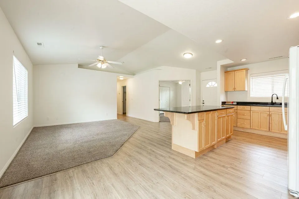 Open-concept living space featuring wood-finish flooring, a kitchen island with a dark countertop, light wood cabinetry, and a ceiling fan