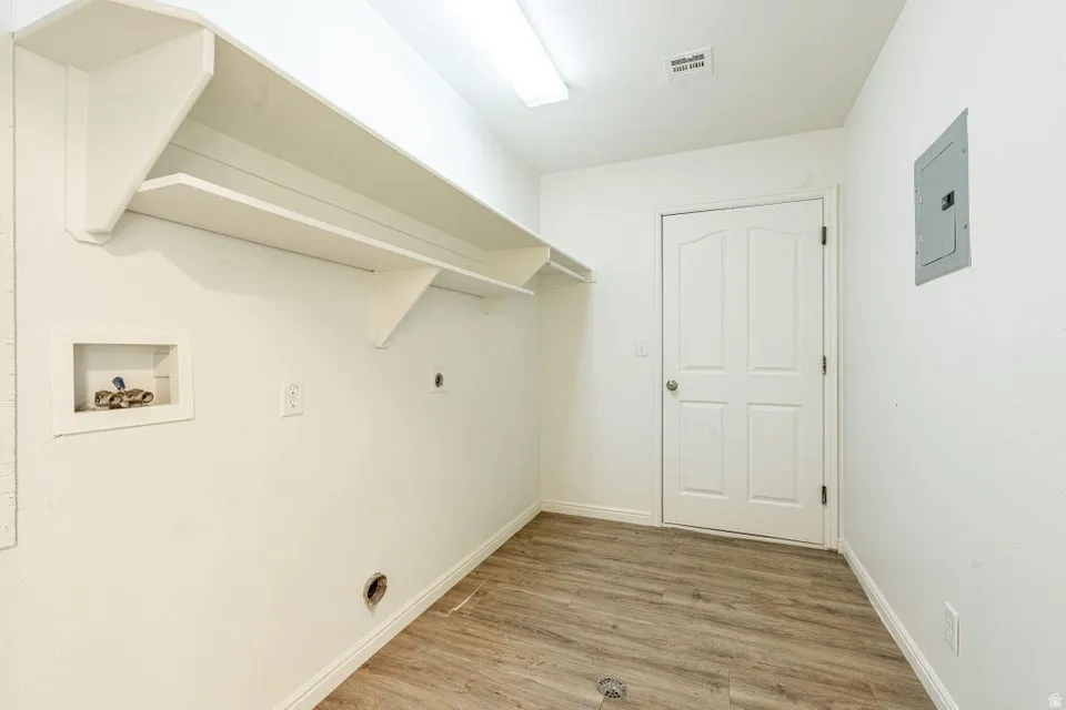 Utility room featuring wood-finish flooring, built-in shelving, white walls, a panel door, and an electrical panel