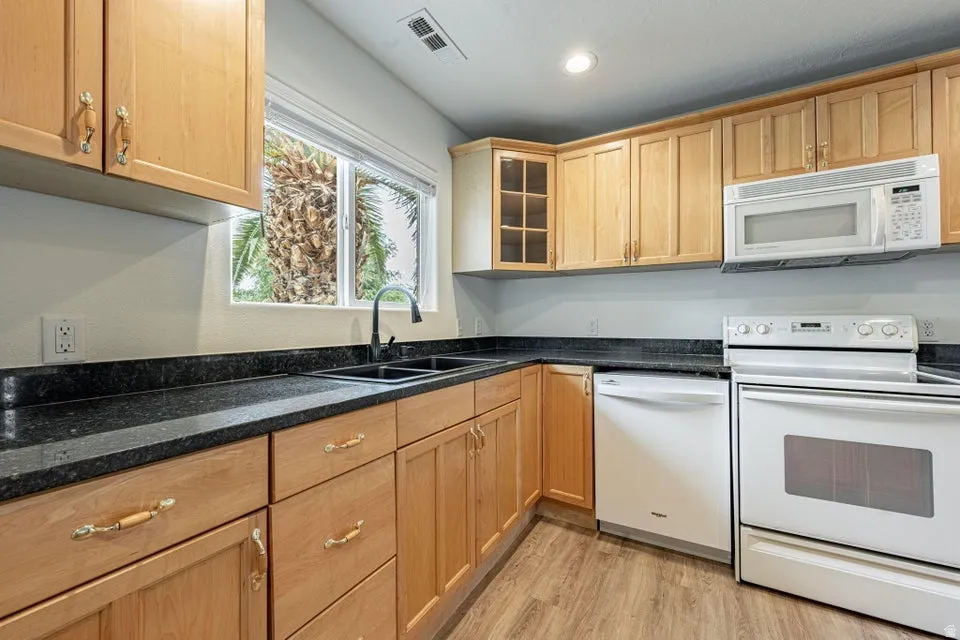 Kitchen featuring natural wood cabinetry, dark countertops, a double basin sink with a gooseneck faucet, and wood-finish flooring