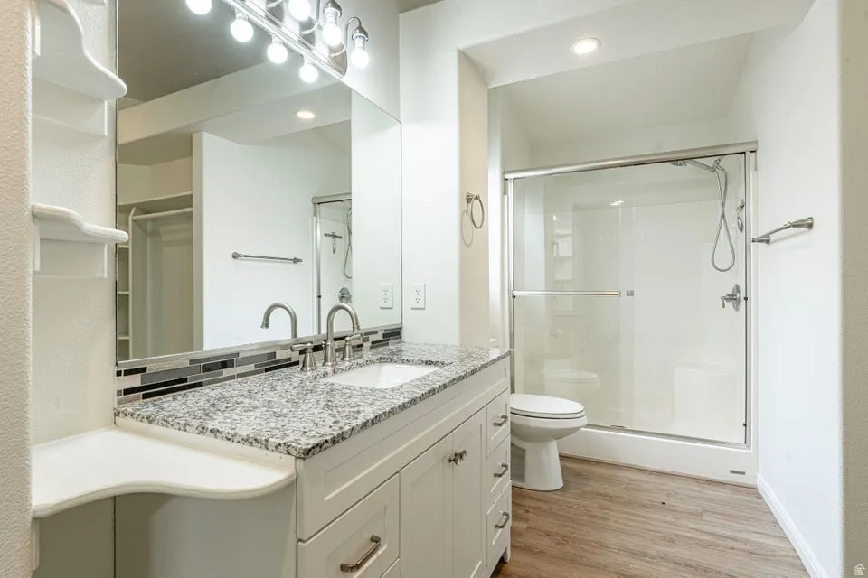 Bathroom featuring a vanity with a white cabinet and granite countertop, a rectangular undermount sink with a brushed nickel faucet, a tiled backsplash, and a large mirror with overhead lighting
