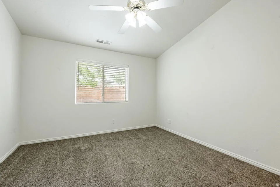 Carpeted interior room with white walls, a single window with horizontal blinds, and a ceiling fan with light fixture
