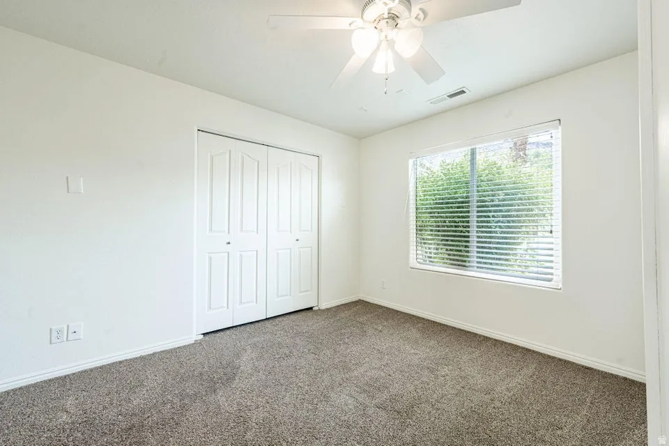 Carpeted room featuring a large window with blinds, a ceiling fan with integrated lighting, and bi-fold closet doors