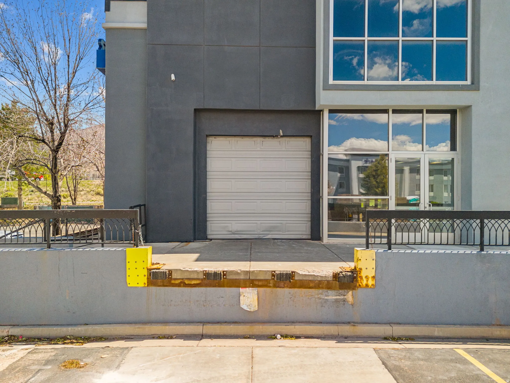 Exterior loading dock with a white roll-up door, reflective glass panels, and an ornate black metal railing