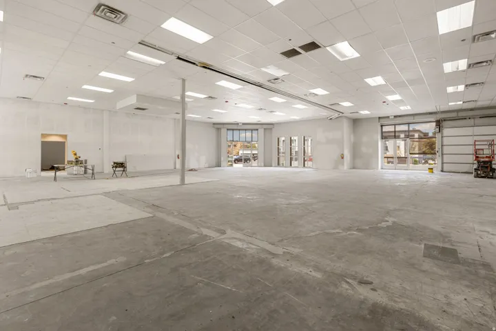 Expansive commercial space featuring a concrete floor, drop ceiling with integrated lighting, multiple storefront windows, and a large roll-up door
