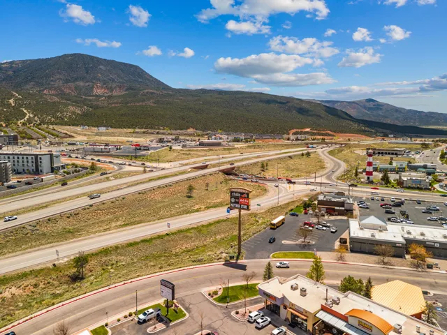 Expansive commercial area featuring multiple retail buildings, a prominent highway interchange, parking facilities, and surrounding natural mountainous terrain