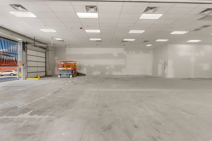 Spacious commercial interior featuring a roll-up garage door, concrete flooring, and a grid ceiling with integrated lighting