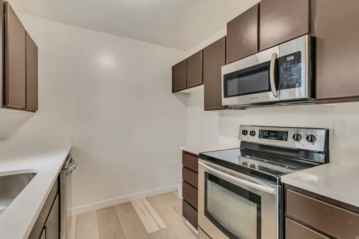 Kitchen featuring dark wood cabinetry, light countertops, stainless steel appliances, and wood-finish flooring