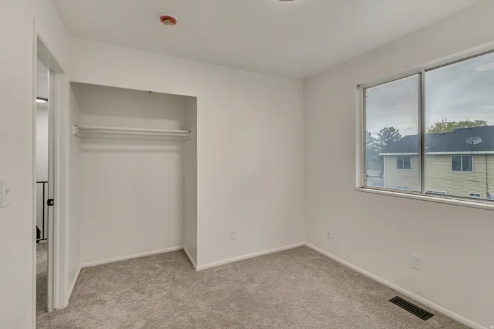 Bright interior space featuring a double window, wall-to-wall carpeting, recessed ceiling light, baseboard trim, and an open closet with a single hanging rod