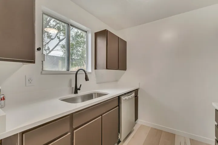 Kitchen area featuring a stainless steel sink with a matte black gooseneck faucet, white countertops, dark brown cabinetry, a stainless steel dishwasher, and light wood-finish flooring