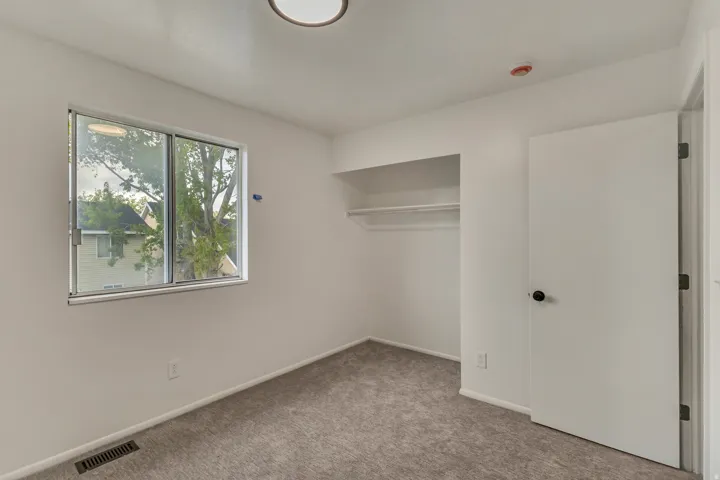 Room featuring gray carpeting, white walls, and a built-in closet with shelving and a hanging rod
