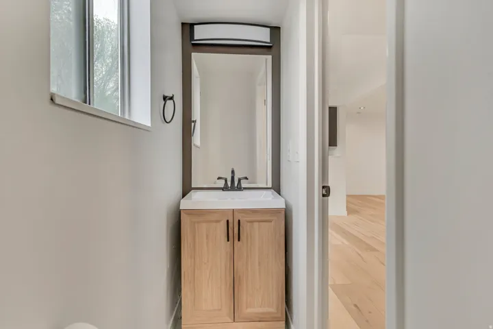 Contemporary vanity with a white rectangular sink, dark bronze faucet, and light wood-finish cabinetry