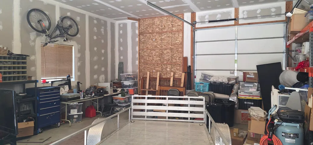 Spacious garage featuring unfinished drywall, exposed ceiling joists, a large garage door, and a single window with blinds