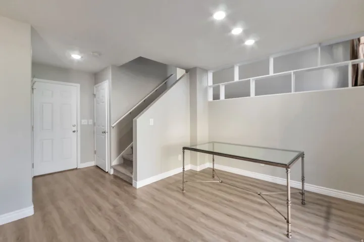 Open-concept space featuring wood-finish flooring, recessed lighting, a white paneled entry door, a carpeted staircase with a white handrail, and built-in shelving