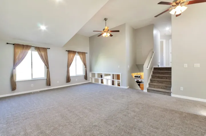 Spacious living area featuring vaulted ceilings, plush carpet flooring, and two ceiling fans