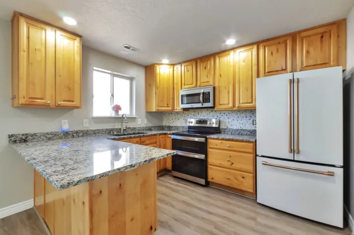 Kitchen featuring light wood cabinetry, light-toned countertops, stainless steel appliances including a microwave and range, and a white refrigerator with gold-tone hardware