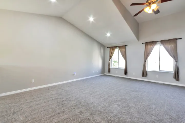 Spacious room featuring vaulted ceilings, recessed lighting, a ceiling fan, two windows, and neutral carpeting