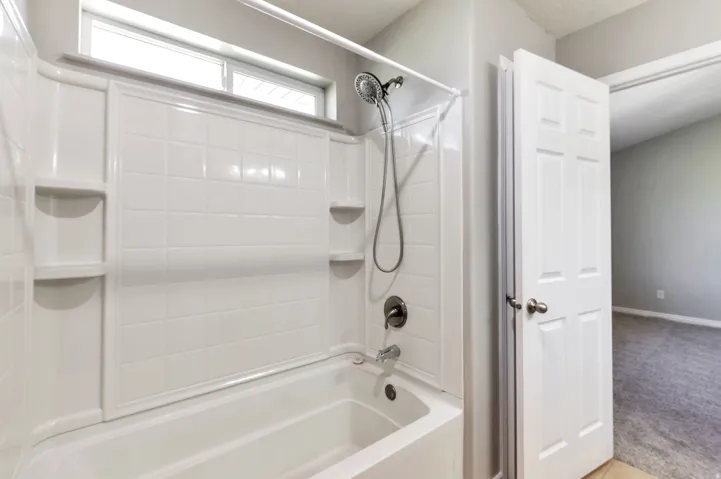 Bathtub and shower combination featuring a white tiled surround with integrated shelving