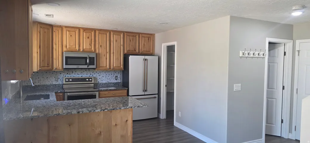 Kitchen featuring natural wood cabinetry, granite countertops, stainless steel appliances, a mosaic tile backsplash, and wood-finish flooring