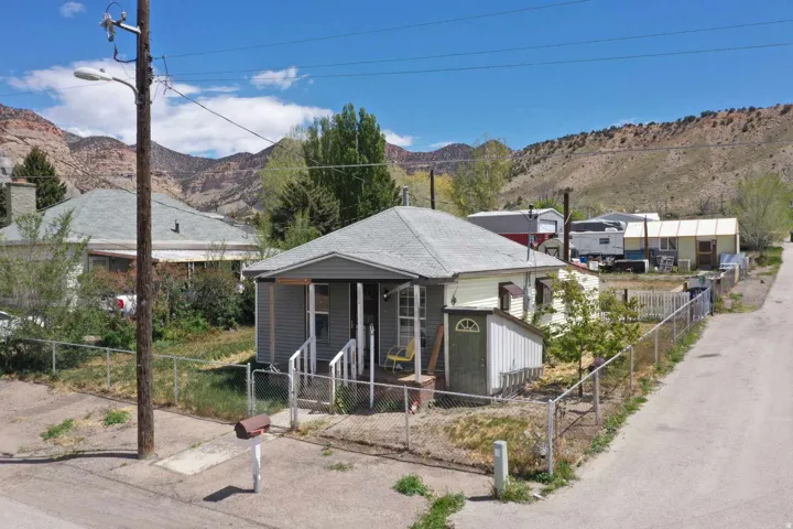 Single-story property featuring a front porch with white railings, a detached shed, a chain-link fence, and a gravel driveway