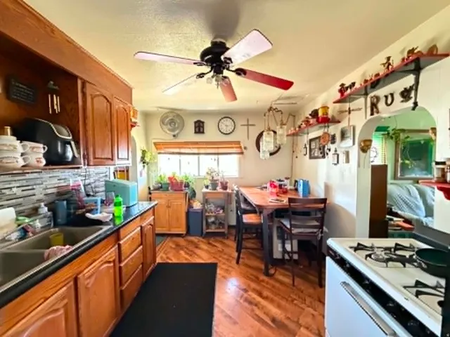 Kitchen space featuring wood-finish flooring, a ceiling fan, and a window with wood blinds