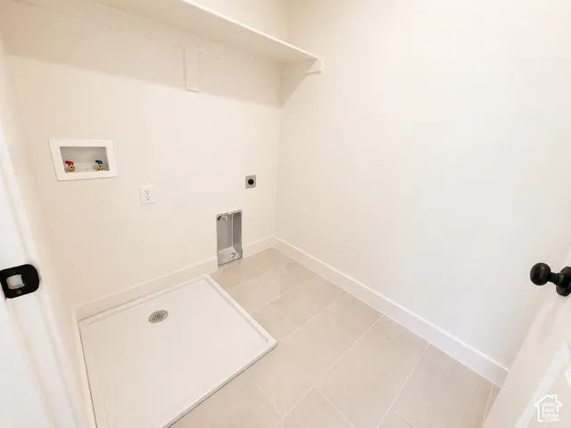 Dedicated laundry area featuring light-toned tile flooring, white baseboards, and a white drain pan