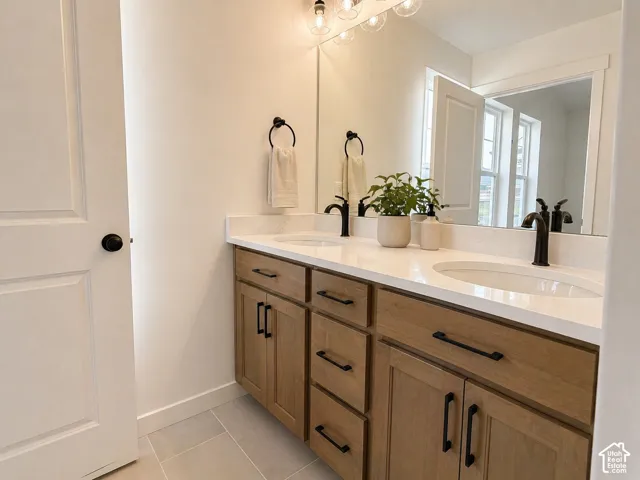 Dual vanity featuring light wood cabinetry, matte black hardware, white countertops with integrated sinks, and a large wall-mounted mirror