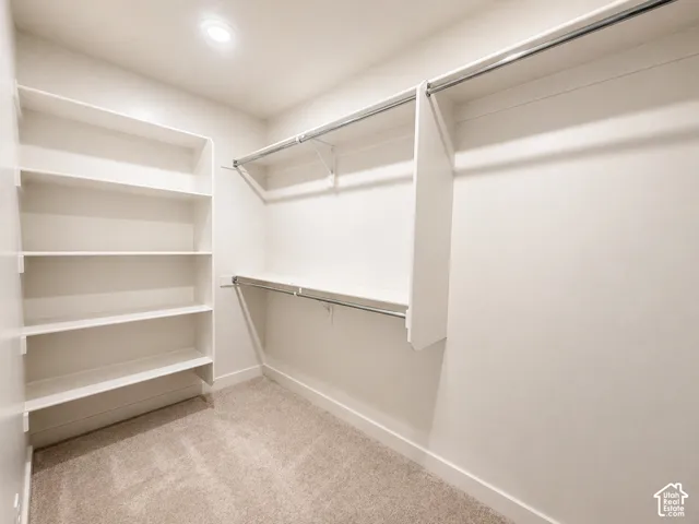 Walk-in closet featuring carpet flooring, built-in shelving, two hanging rods, and recessed lighting