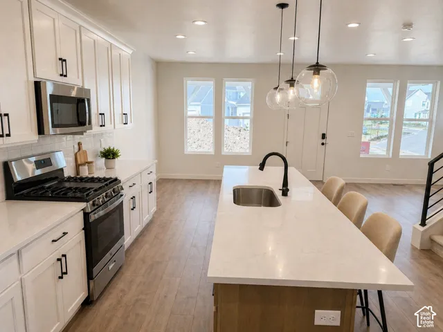 Open-concept kitchen featuring white shaker cabinetry, stainless steel appliances, a subway tile backsplash, and a large island with a surface-mount sink and pendant lighting