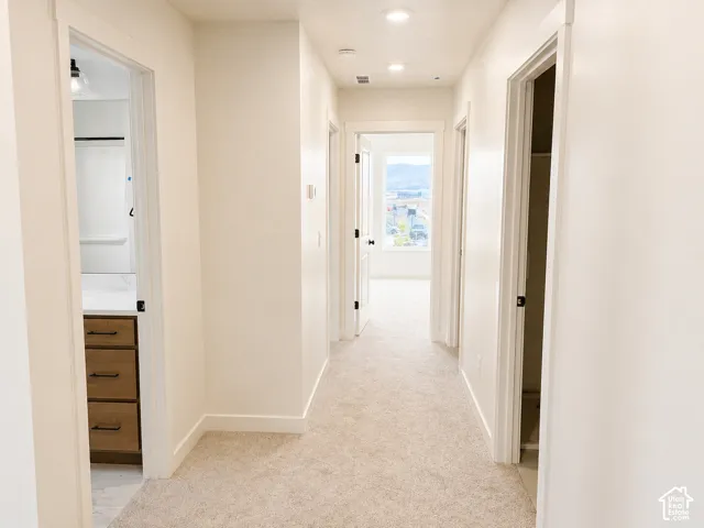 Carpeted hallway featuring bright white walls, recessed lighting, and multiple doorways with dark hardware