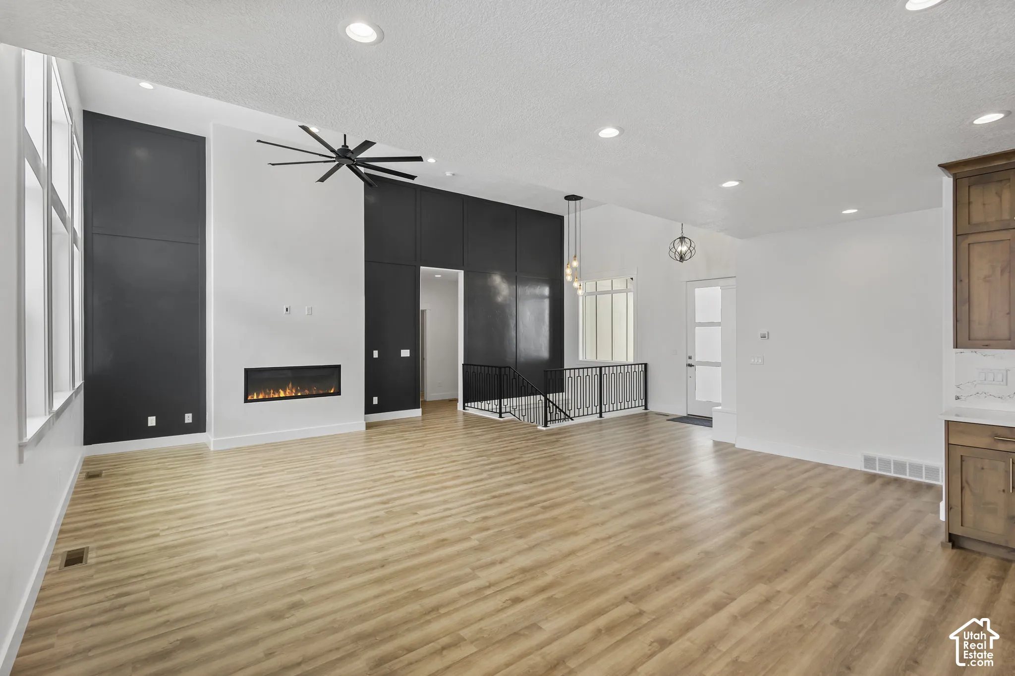Vaulted ceiling great room featuring a linear electric fireplace, wood-finish flooring, a contemporary ceiling fan, and tall windows
