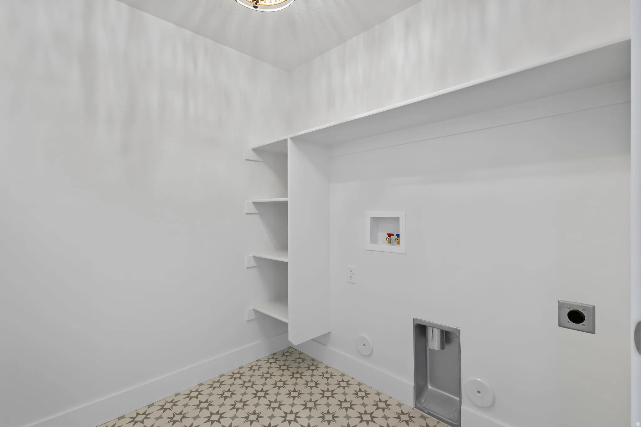 Laundry space featuring patterned floor tiles, built-in shelving, an overhead light fixture, and white baseboards