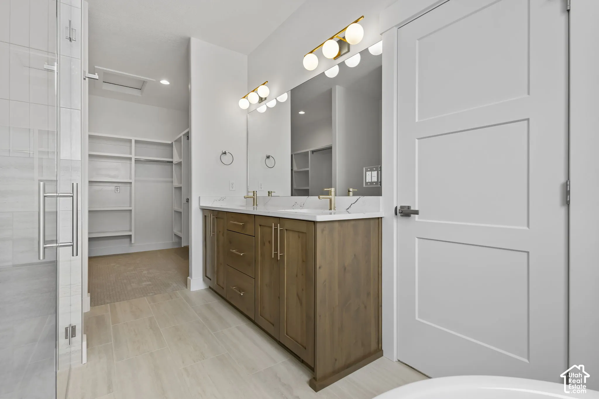 Bathroom featuring a double vanity with wood-finish cabinetry, white countertops, dual undermount sinks, and gold-finish fixtures