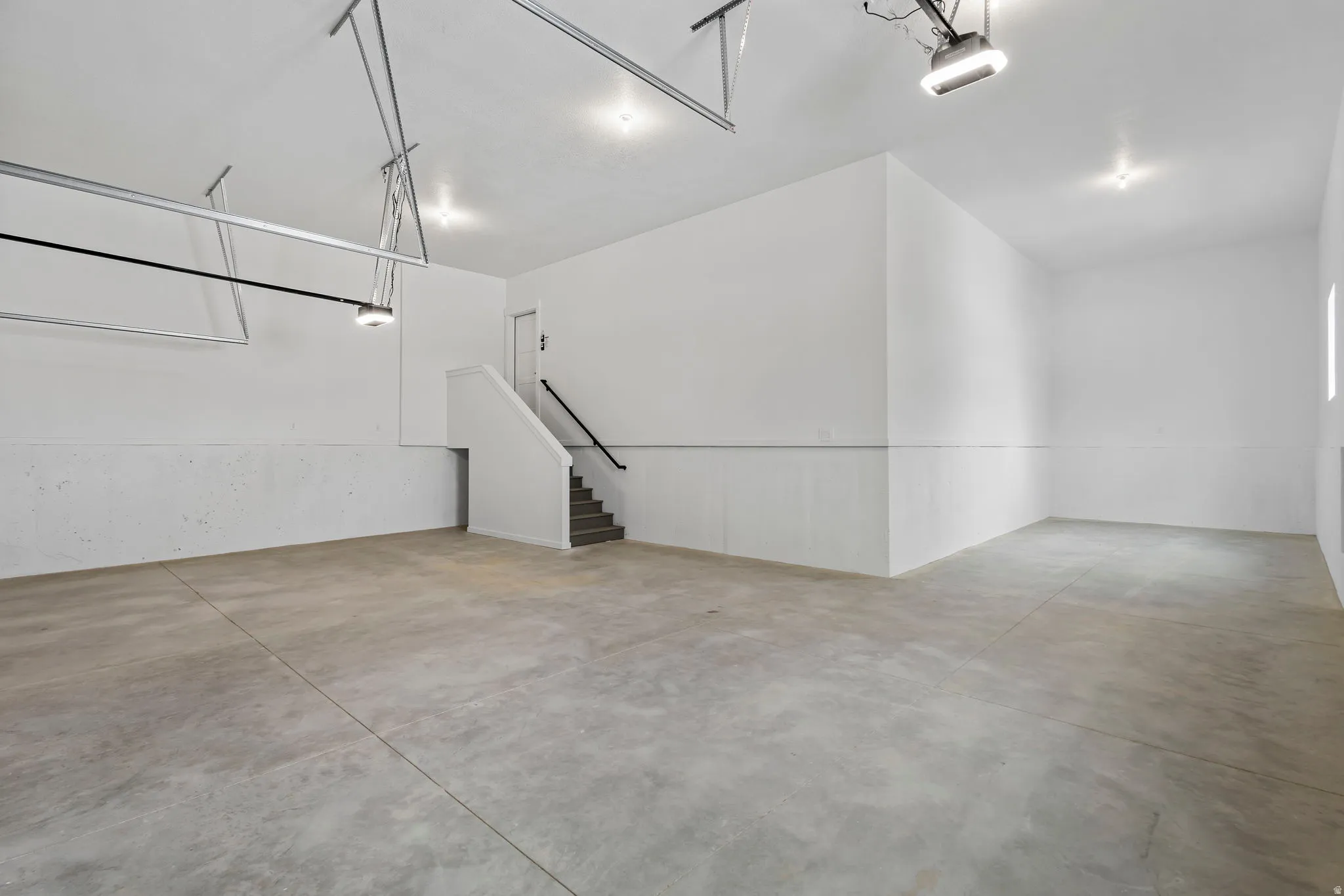 Spacious garage featuring a concrete floor, bright white walls, recessed lighting, and a built-in staircase with a handrail