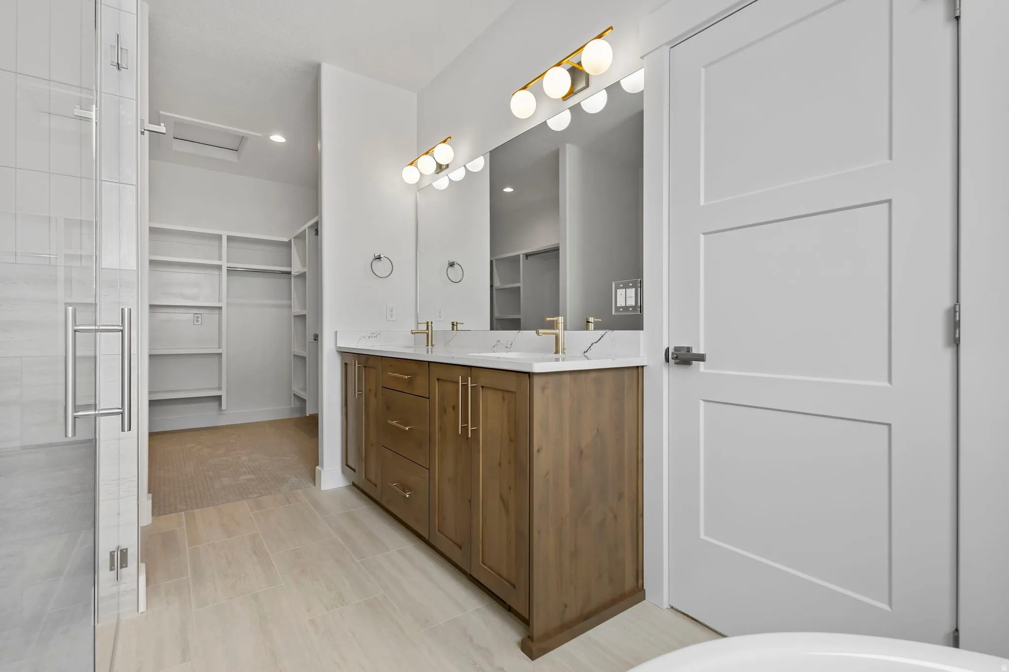 Bathroom featuring a double vanity with wood-finish cabinetry, white countertops, dual undermount sinks, and gold-finish fixtures